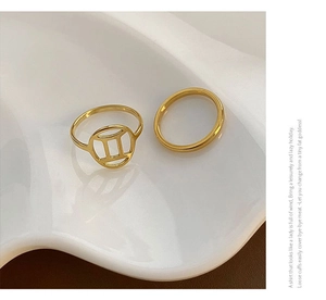 Detailed shot of two-piece gold Gemini zodiac rings on a white ceramic tray