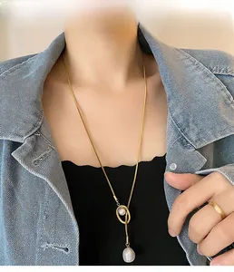 Detail of long gold necklace with a large baroque pearl pendant on a denim-clad model