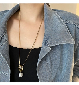 Detail of gold snake chain necklace featuring a baroque pearl pendant on a denim jacket model