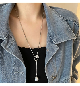 Close-up of a silver necklace with a baroque pearl pendant worn on a denim jacket