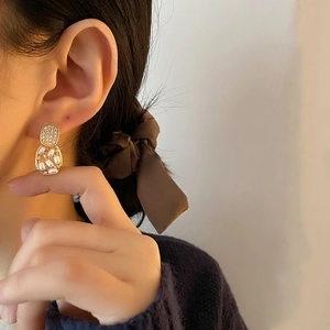 Elegant gold-tone geometric pearl earrings with diamond accents on a female model