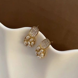 Elegant geometric gold earrings with micro-set zircons and pearls on white wavy ceramic
