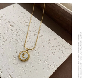 Detailed shot of gold moon pendant necklace with white shell on textured stone surface