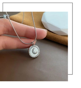 Macro detail of silver moon pendant on snake chain over premium leather background