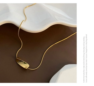 Detailed close-up of a polished gold-tone irregular pendant on a sleek snake bone chain