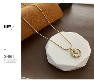 Close-up of gold snake chain with crescent moon shell pendant on white geometric stone