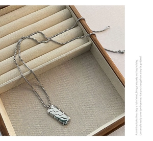 Detailed close-up of a silver geometric textured pendant necklace in a wooden jewelry box