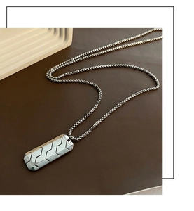 Macro detail of silver rectangular pendant with geometric tire pattern on ball chain