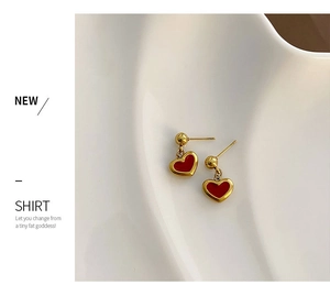 Detail view of gold earrings with red heart pendants on a textured white tray