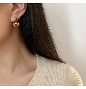 Close-up of elegant gold and red heart drop earrings worn by a model in beige knitwear