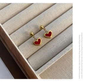 Close-up of heart-shaped red enamel drop earrings with gold metallic frames and ball studs