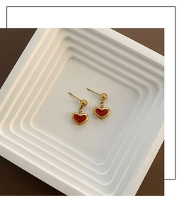 Close-up of minimalist red heart earrings with golden beads on a modern display stand