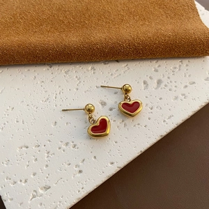 Minimalist red heart earrings in gold finish set against a textured elegant background