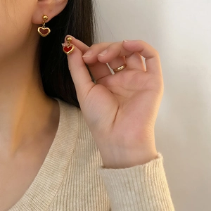 Minimalist gold heart earrings with red enamel finish worn by a model in soft lighting
