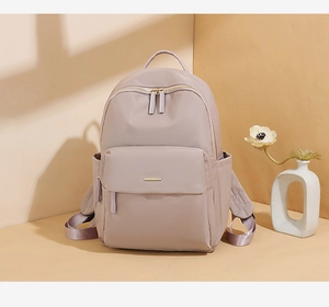Detail of waterproof nylon backpack showing front zip pocket and gold metal brand plate