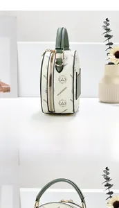 Detailed side view of round crossbody bag with monogram pattern and green accents