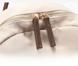 Gros plan détaillé des fermetures éclair dorées sur un sac à dos en nylon beige