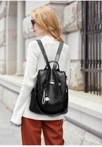 Side view of a black oxford fabric backpack with a cute bear charm on a city street