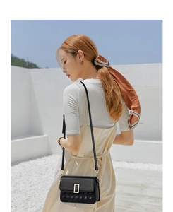 Detail of a black quilted crossbody bag with a gold rectangular buckle on white background