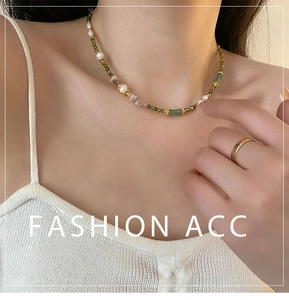 Detail of pearl necklace with green bamboo pendant and beads on white knit top