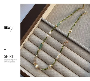 Detail view of pearl and green gemstone necklace with gold clasp in a velvet jewelry box