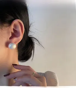 Close-up of a large round white pearl earring worn by a model in soft lighting