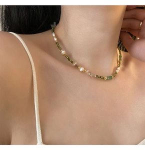Detail of green beaded necklace with white pearls and gold accents on a model's collarbone