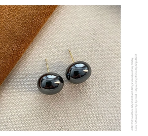Detailed close-up of polished gunmetal spherical stud earrings with gold needles