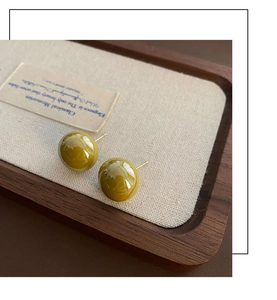 Close-up of olive green pearl stud earrings on a vintage wooden tray and linen pad