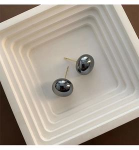 Detailed view of deep grey spherical stud earrings on a white geometric display tray