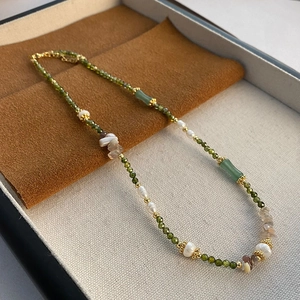 Vintage pearl necklace with green faceted beads and gold accents on a suede tray