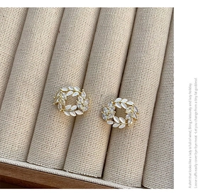 Detail of elegant gold wheat-shaped wreath earrings with pearlescent leaves and zircons