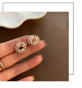 Close-up of elegant gold wreath earrings with white enamel leaves and sparkling crystals