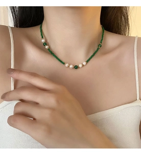Detail of beaded necklace with green agate and white pearls worn on a model's neck