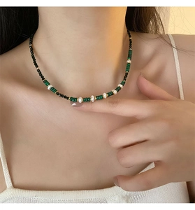 Detail of beaded necklace with green malachite, white pearls and gold accents on a model
