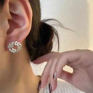Elegant gold leaf wreath earrings with white shell and zircon accents on a model