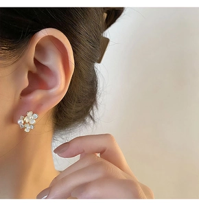 Détail du boucle d'oreille fleur en émail blanc avec perles sur l'oreille du mannequin