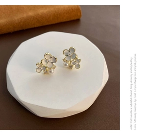 Détail de boucles d'oreilles fleurs en émail blanc, perles et finition dorée