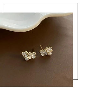 Détail de boucles d'oreilles fleurs en émail avec perles et base dorée sur fond texturé