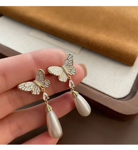 Detailed close-up of French-style butterfly drop earrings with white pearls and gold trim