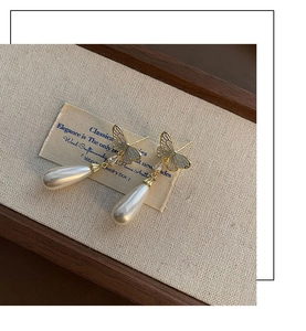 Close-up of elegant gold butterfly drop earrings with white pearl dangles on a jewelry tray