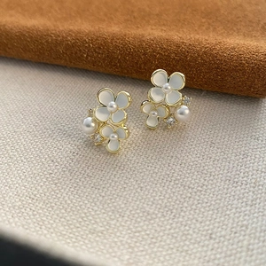 Boucles d'oreilles fleurs dorées avec pétales blancs et perles sur tissu texturé