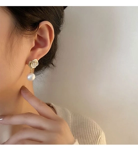Primo piano di eleganti orecchini a rosa dorata e perla indossati da una modella