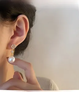 Detail view of sparkling diamond pearl drop earrings on model in soft golden lighting