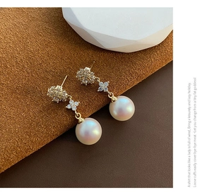 Close-up of elegant pearl drop earrings with sparkling flower-shaped zirconia in gold finish