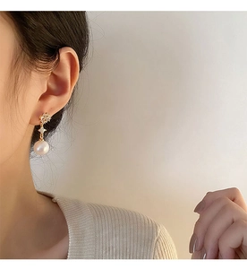 Close-up of elegant pearl drop earring with gold floral diamond stud on model