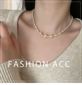 Detail shot of elegant white gradient pearl necklace on model with beige knitwear