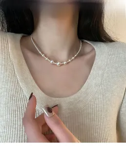 Detail of gradient pearl necklace on model wearing a beige knit top for styling