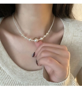 Detail of gradient mermaid pearl necklace worn on neck with white knit sweater