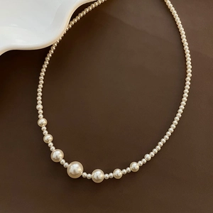 Elegant titanium steel necklace with graduated cream pearls on a dark leather surface